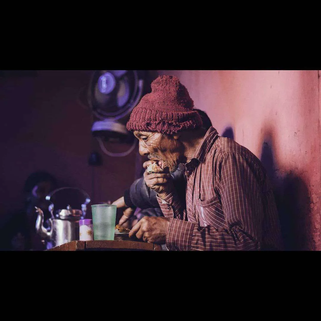 A man eating at a tea stall, lit by warm market light